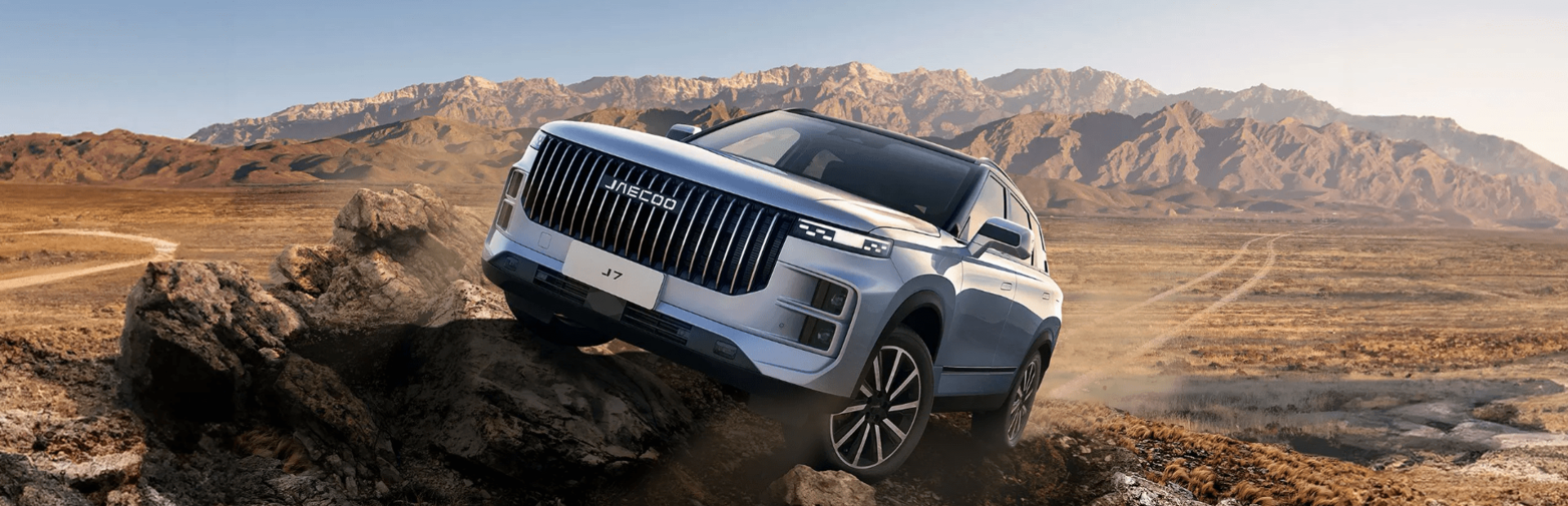 Silver SUV driving over rocky terrain with mountains in the background.